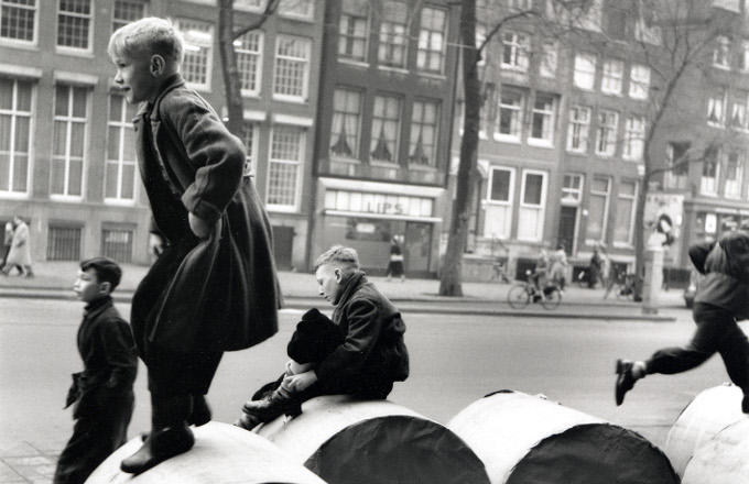 Amsterdamse jongens spelen buiten op papierrollen die voor de krant bestemd zijn Amsterdamse jongens spelen buiten op papierrollen die voor de krant bestemd zijn
